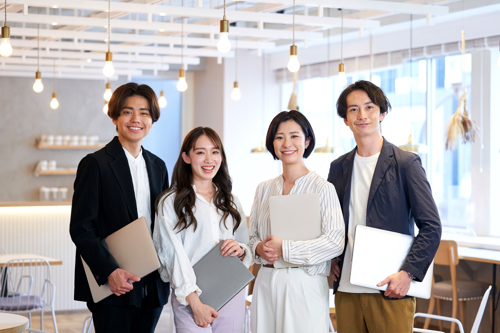 明るい共用スペースでノートパソコンを抱えて立つ働く人たち