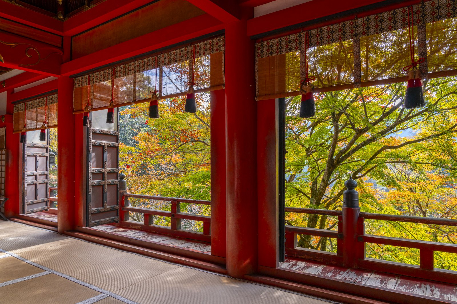談山神社の拝殿の回廊。朱の柱と簾ごしに山の木々が見える