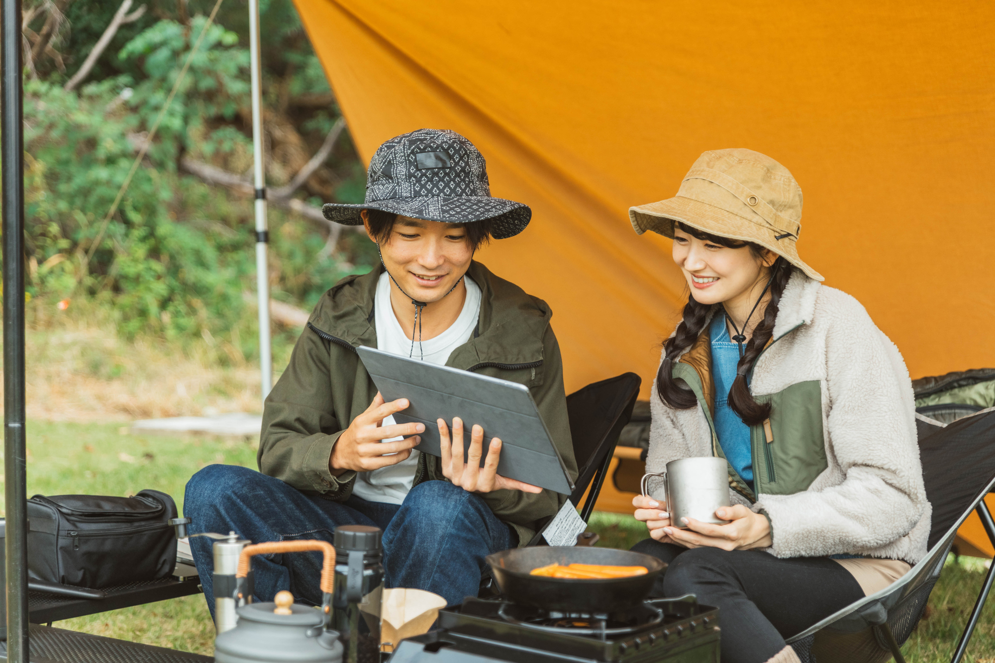 秋冬のキャンプ場でタブレットを見る二人