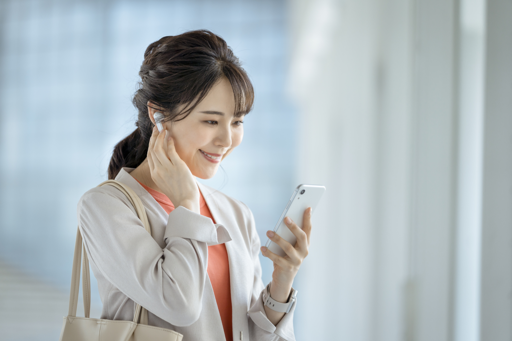 イヤホンをつけてスマートフォンの画面を見る女性