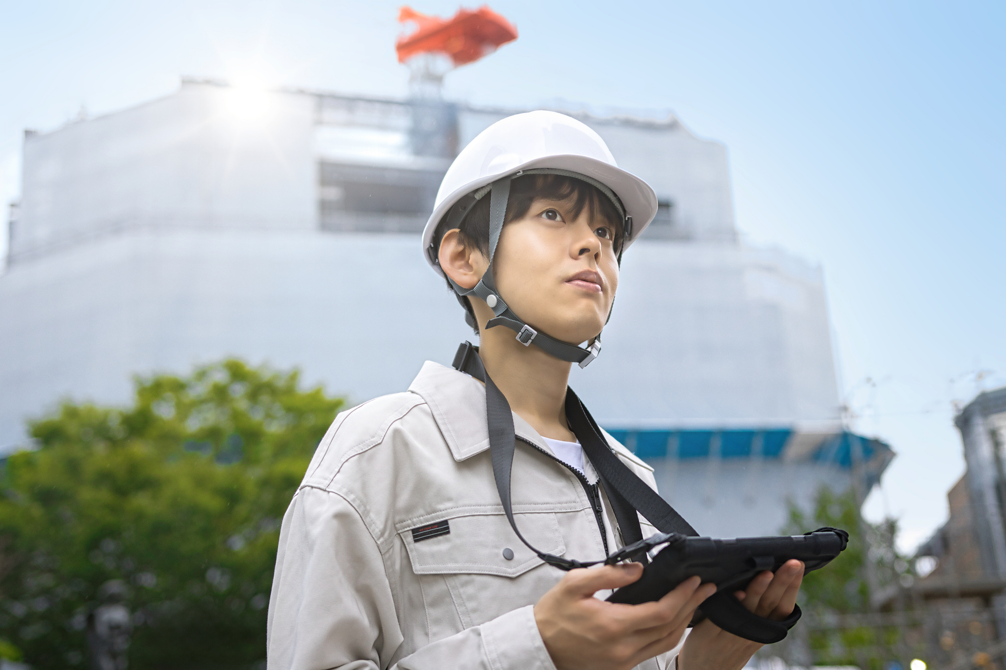 工事現場でタブレットを手に建物を見上げる作業服の男性