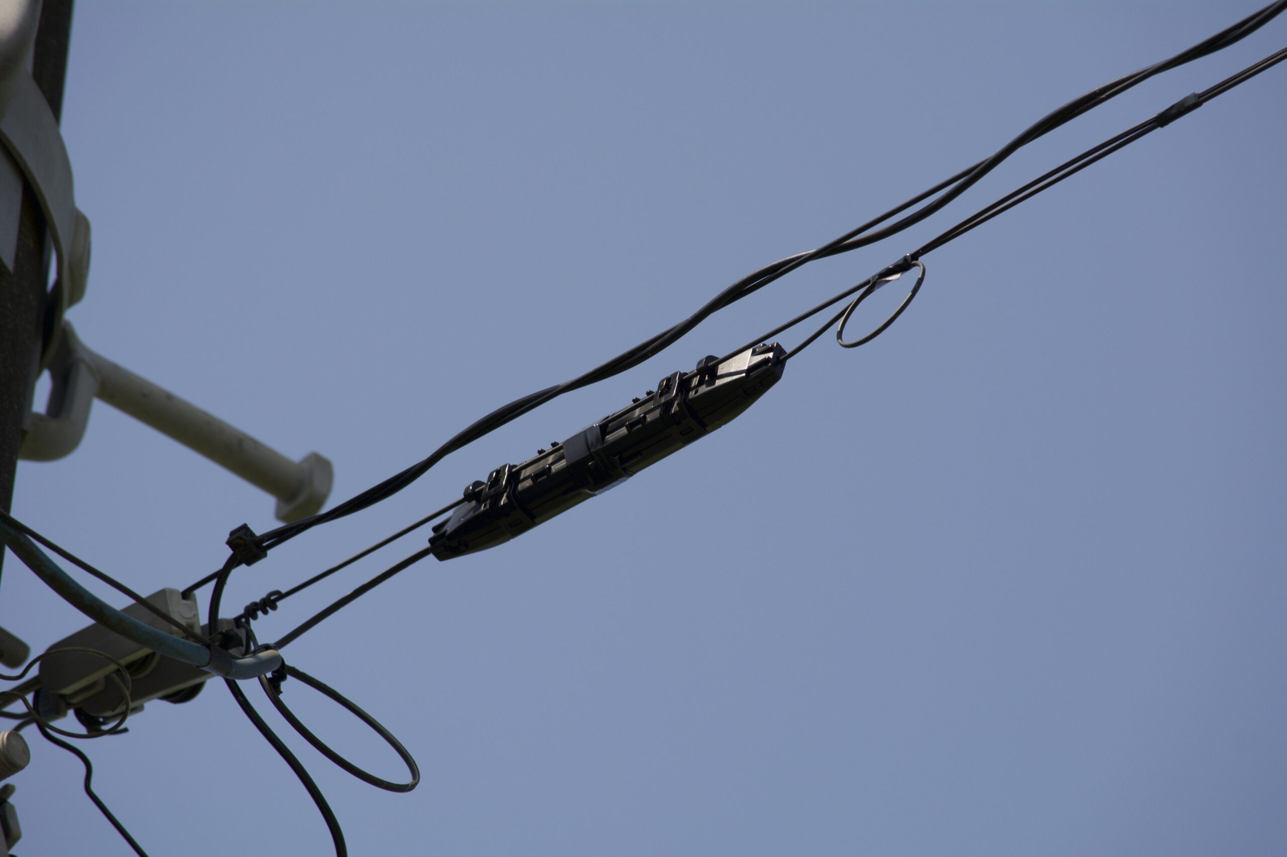 青空を背景に電柱から張られた通信ケーブルと接続箱