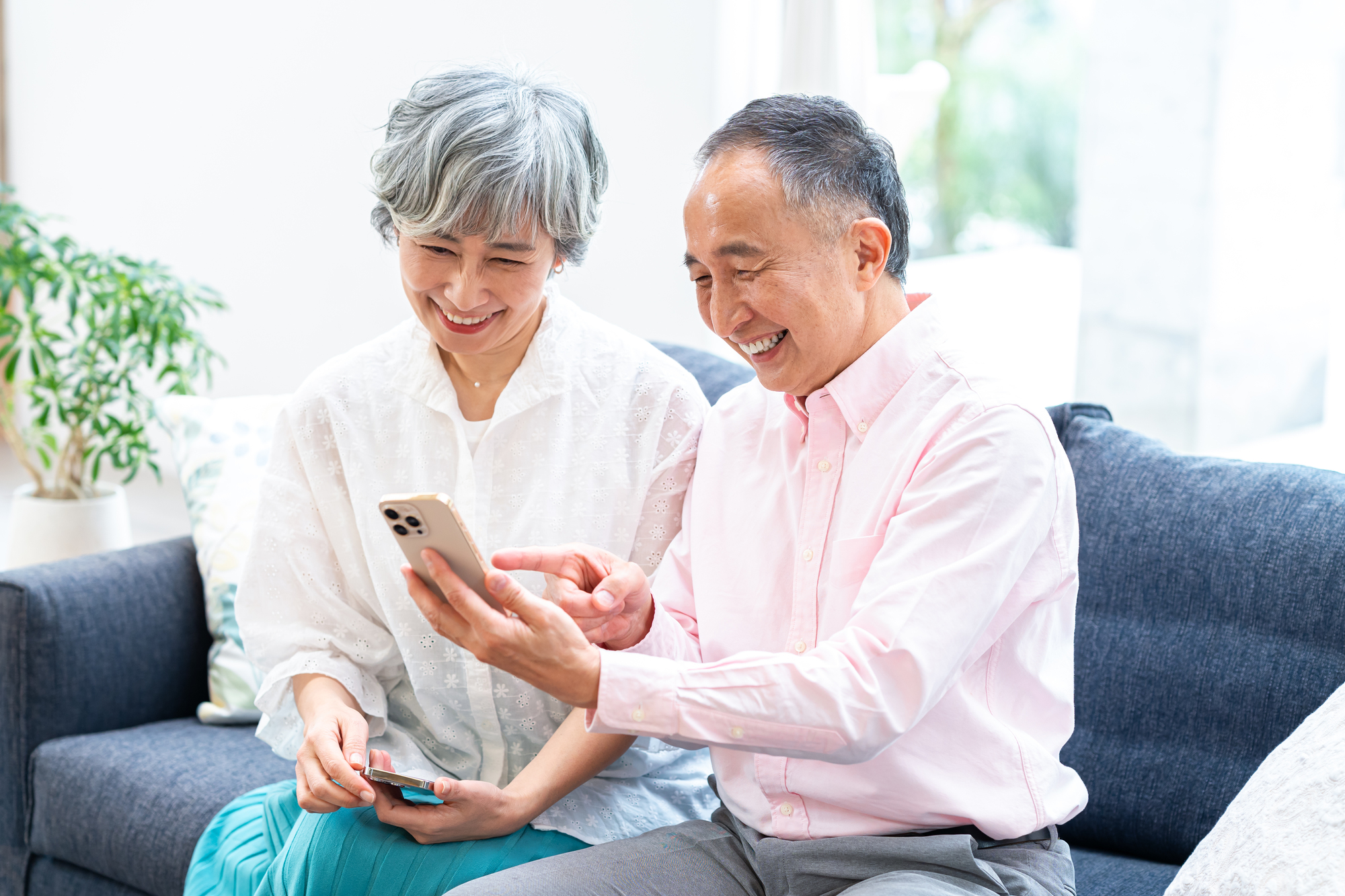 リビングのソファでスマートフォンの画面を一緒に見る高齢の夫婦