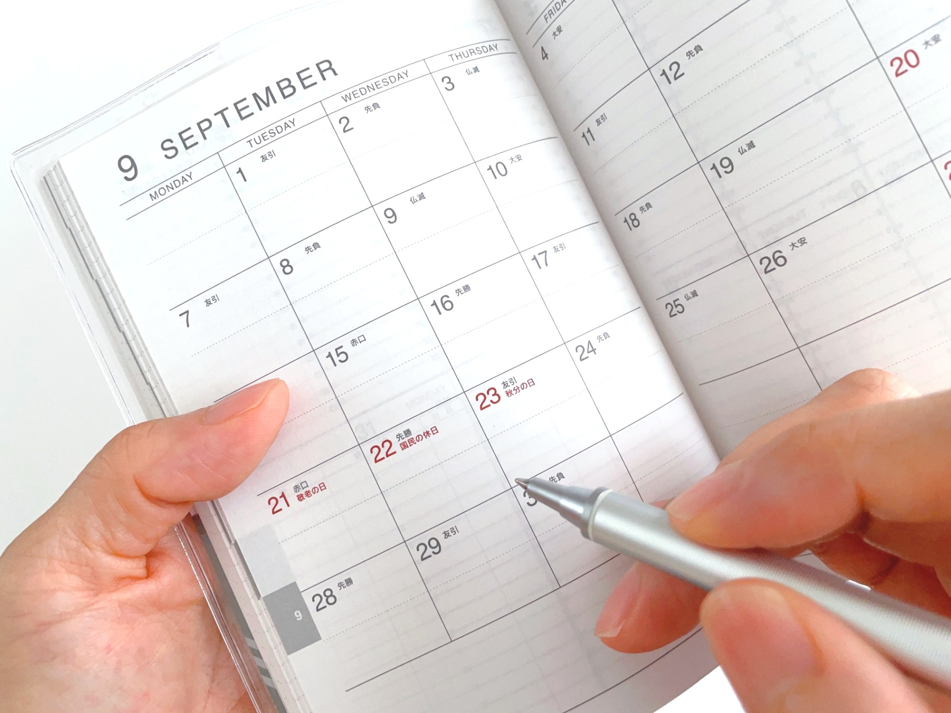 9月のスケジュール帳に予定を記入する手元（PIXTA）