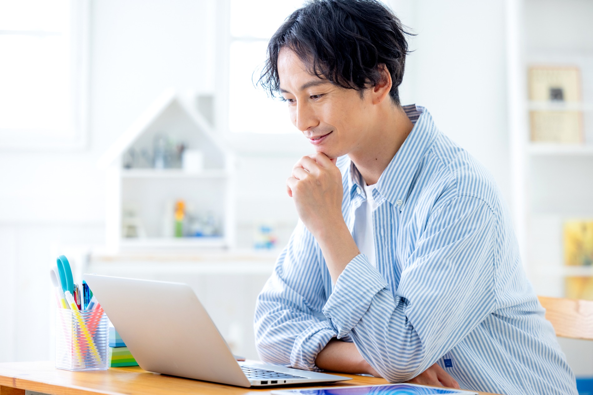 自宅の机でノートパソコンに向かい考え込む男性