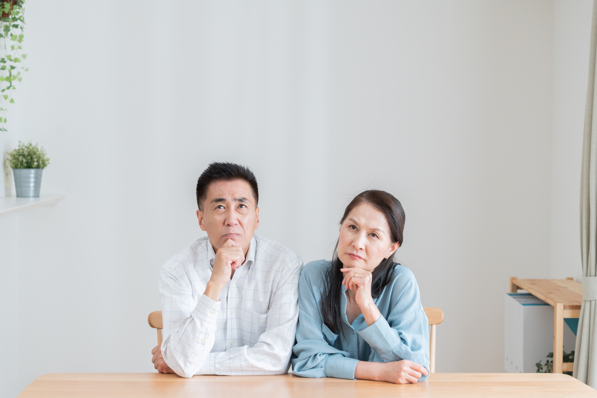 ダイニングテーブルで考えごとをしている高齢の夫婦