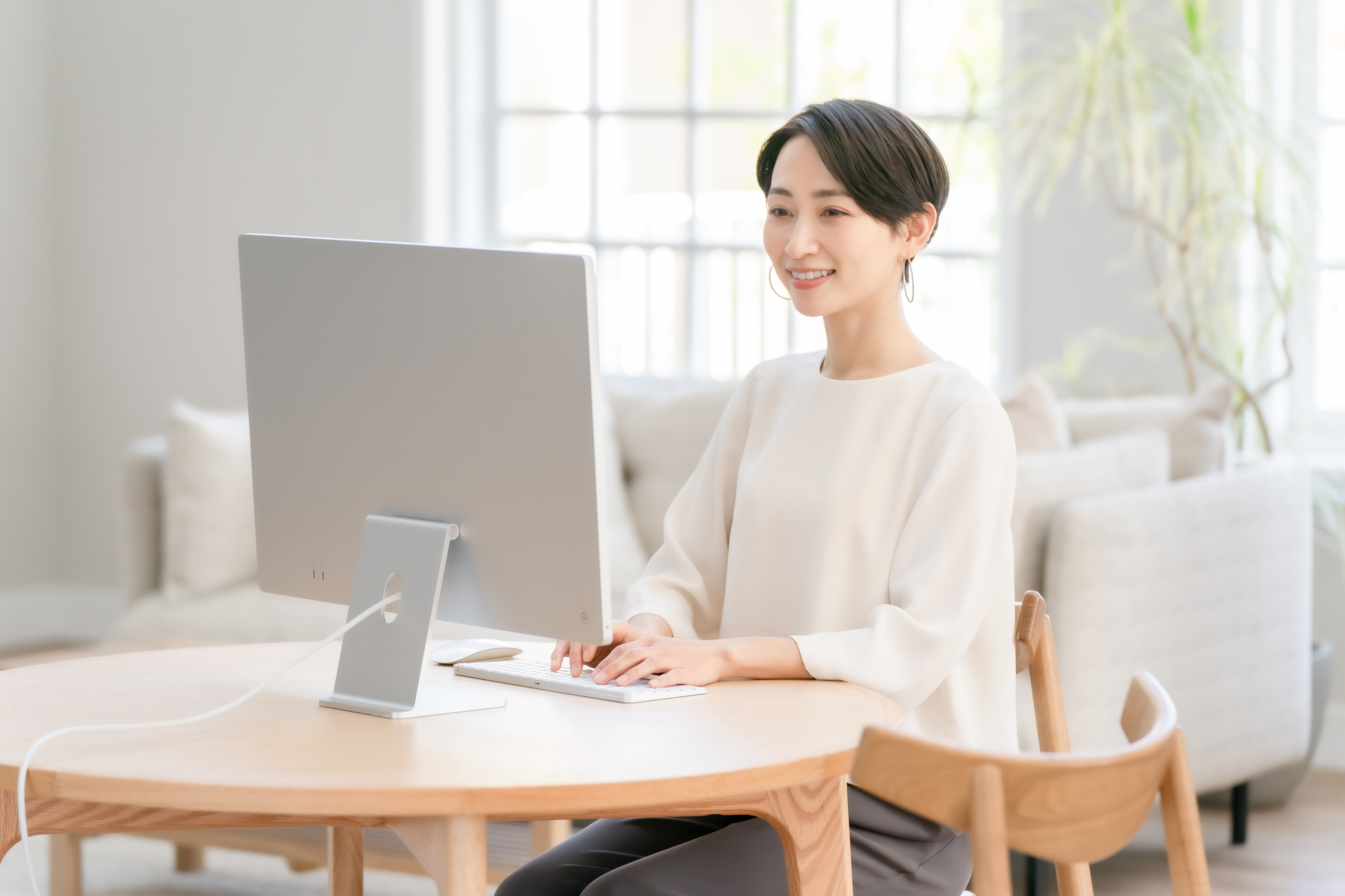 自宅の居室で据え置き型のパソコンに向かって作業している女性