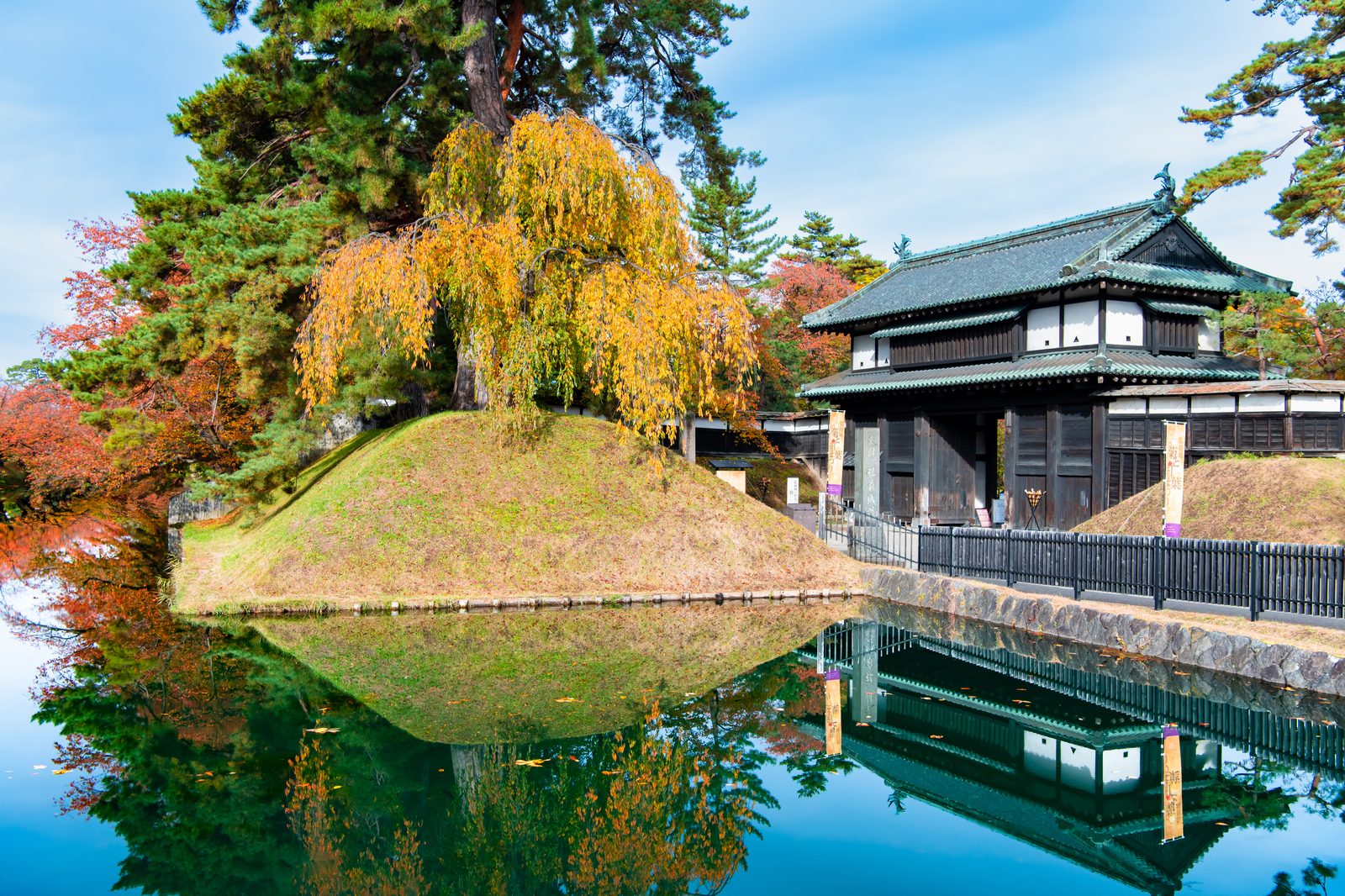 紅葉に囲まれた弘前城の追手門と、水面に映る三の丸の景色