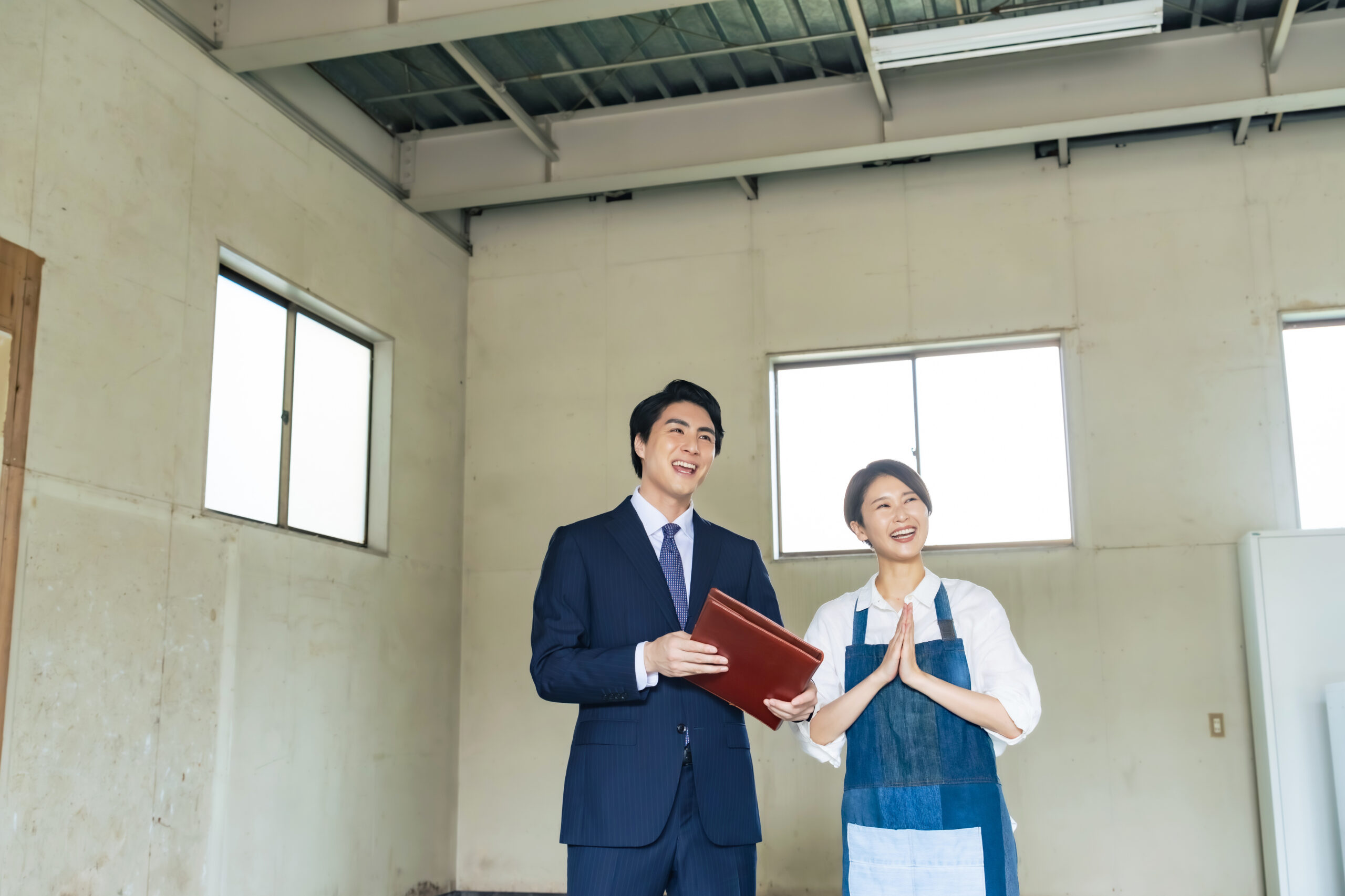 内装前の物件を見上げる事業主と、書類を持った不動産会社の担当者