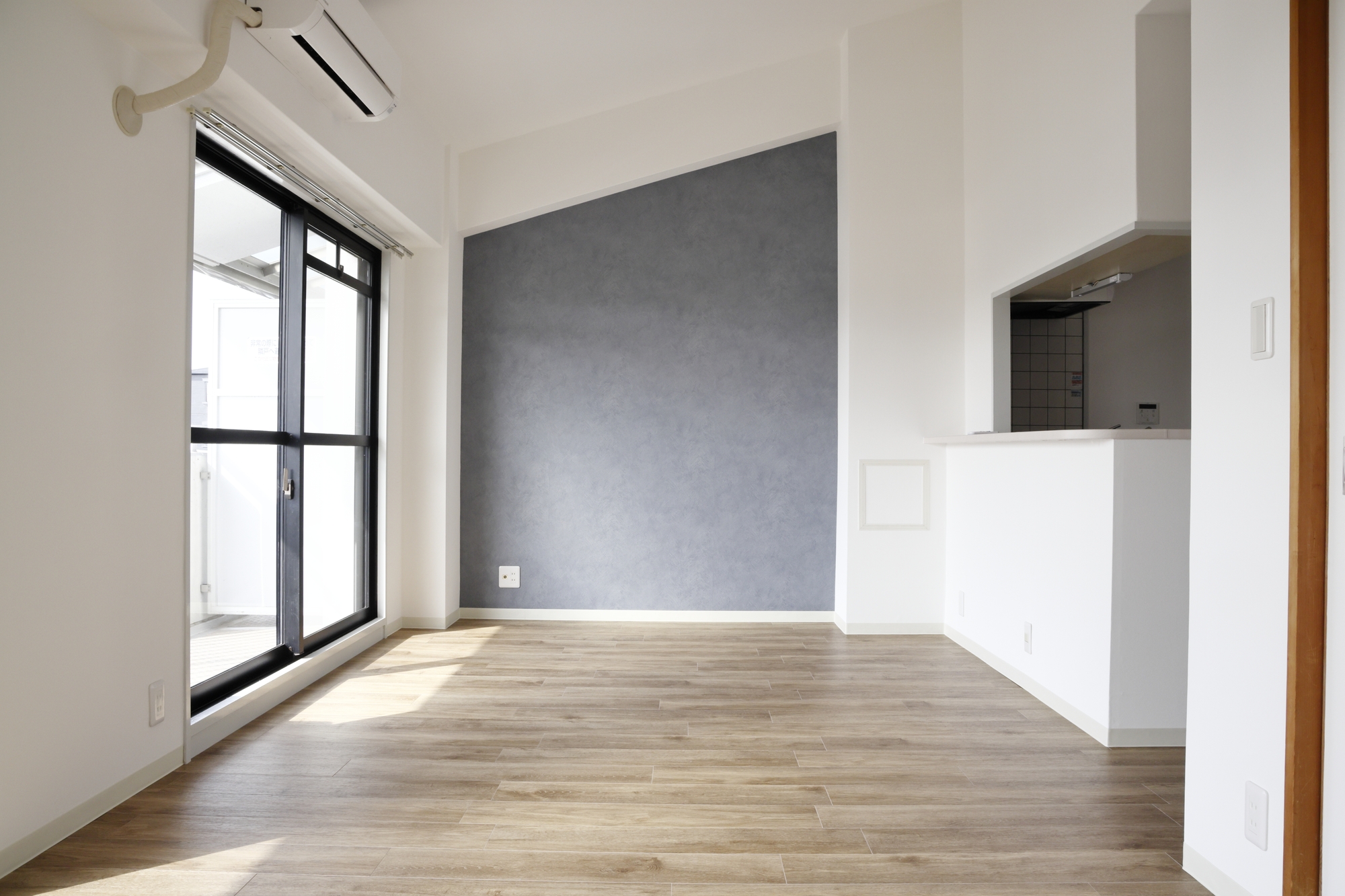 入居前の賃貸住宅の空室。フローリングの居室と掃き出し窓、壁に取り付けられたエアコン