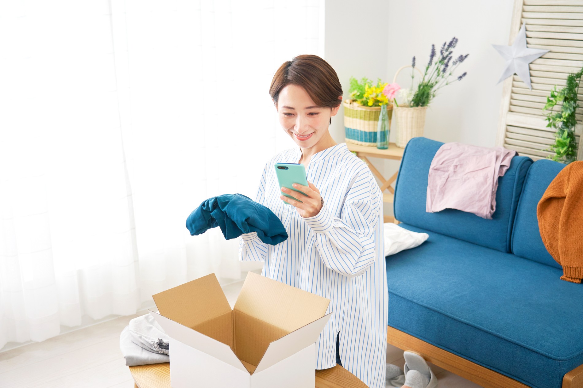 段ボール箱の前でスマートフォンを持ち、手に取った洋服を撮影する人