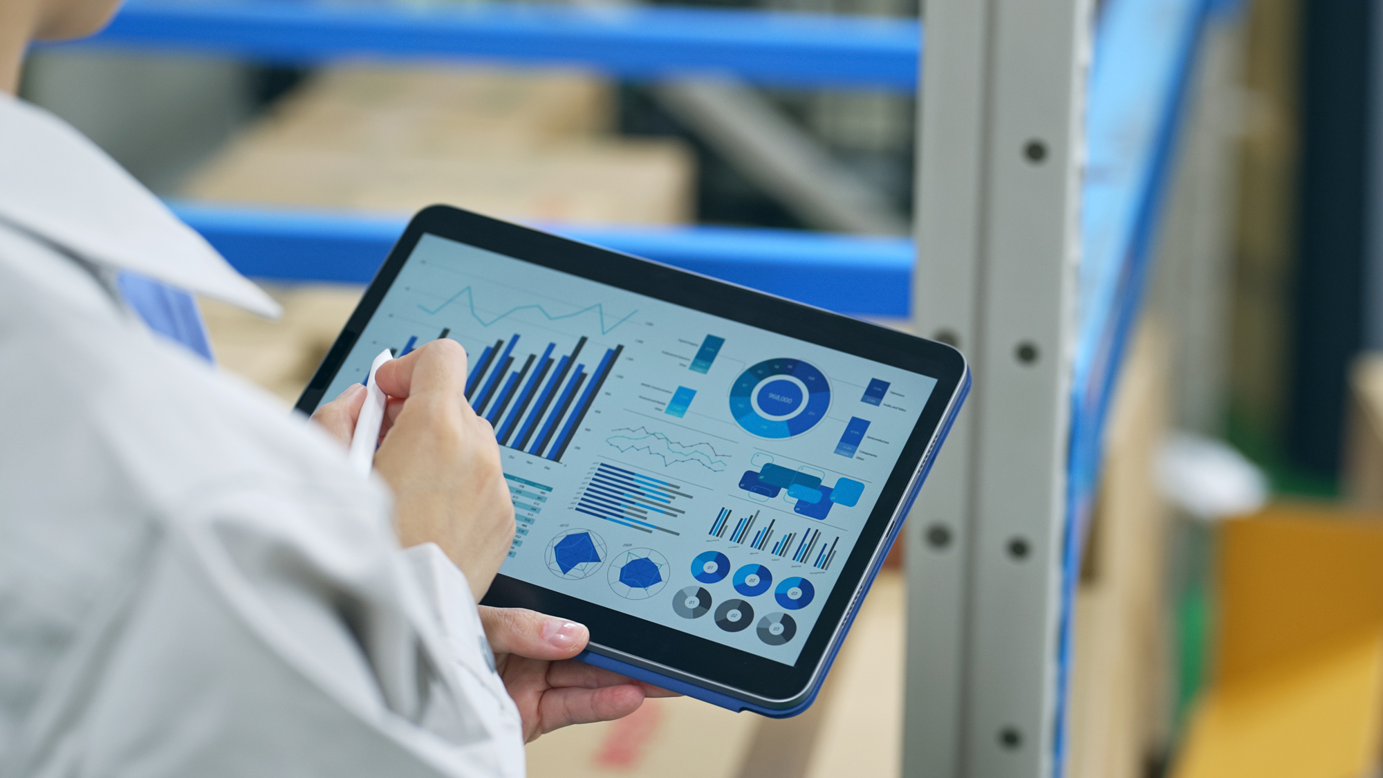 倉庫の棚の前でタブレットの画面を見ながら記録を入力する作業員の手元