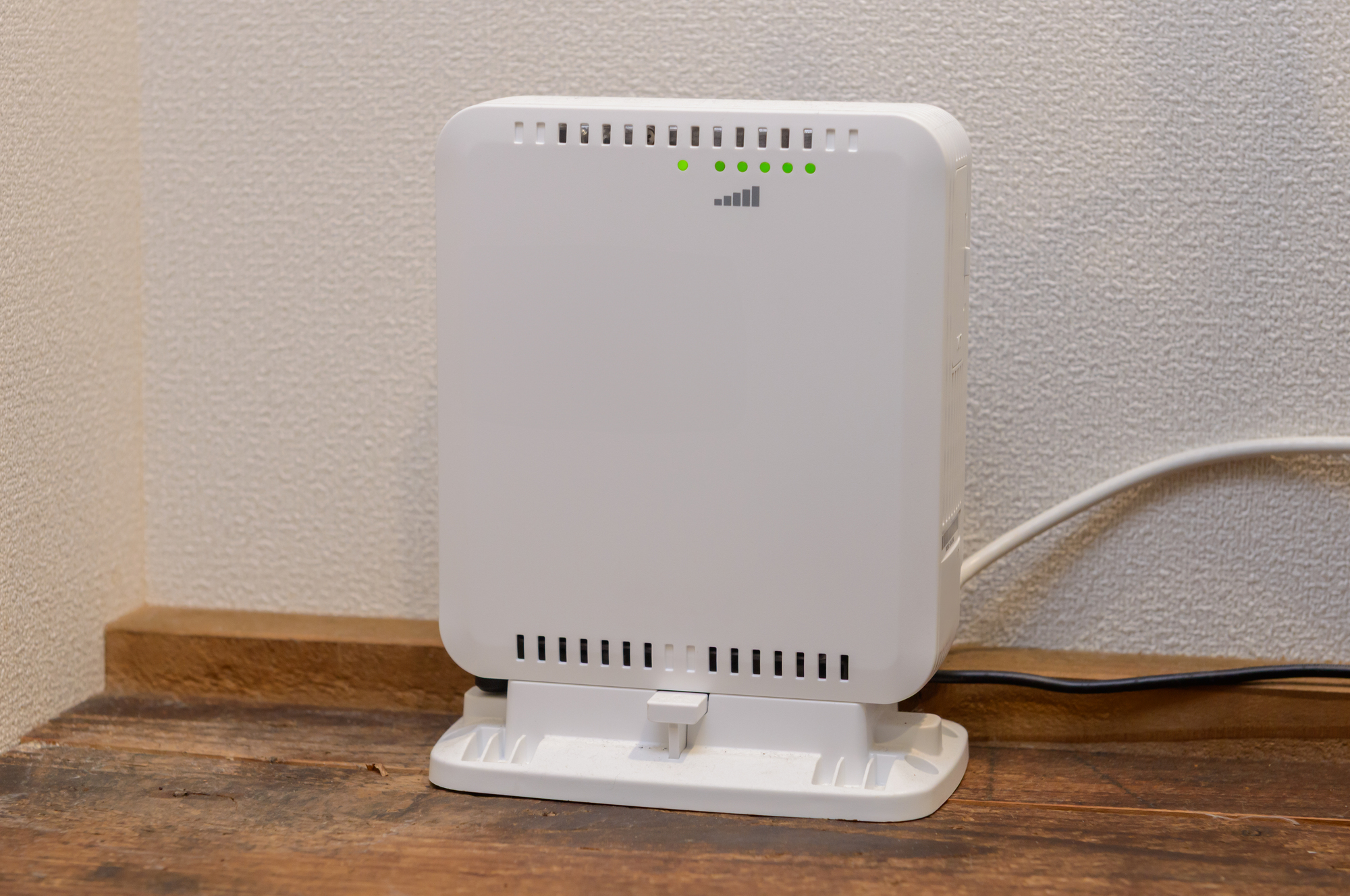 部屋の棚に置かれた据え置き型のホームルーターと、背面から伸びる電源コード
