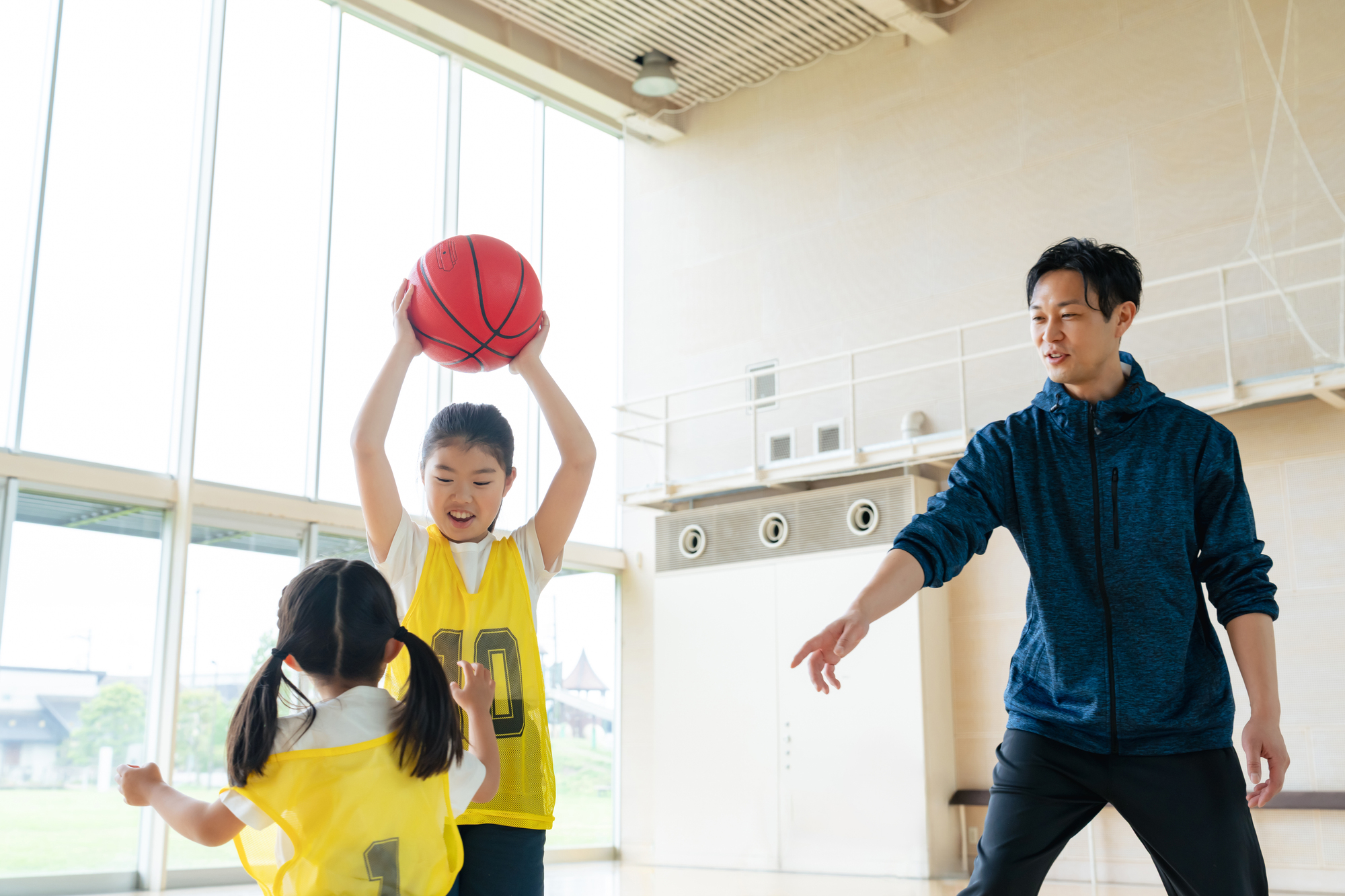 体育館で子どもにシュートの形を教えるコーチ