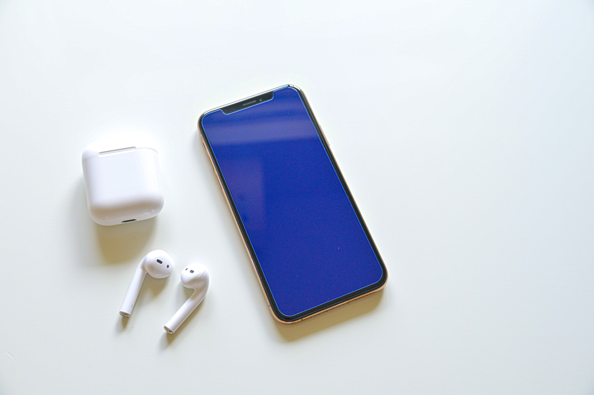 白い机の上に並べたスマートフォンとワイヤレスイヤホン