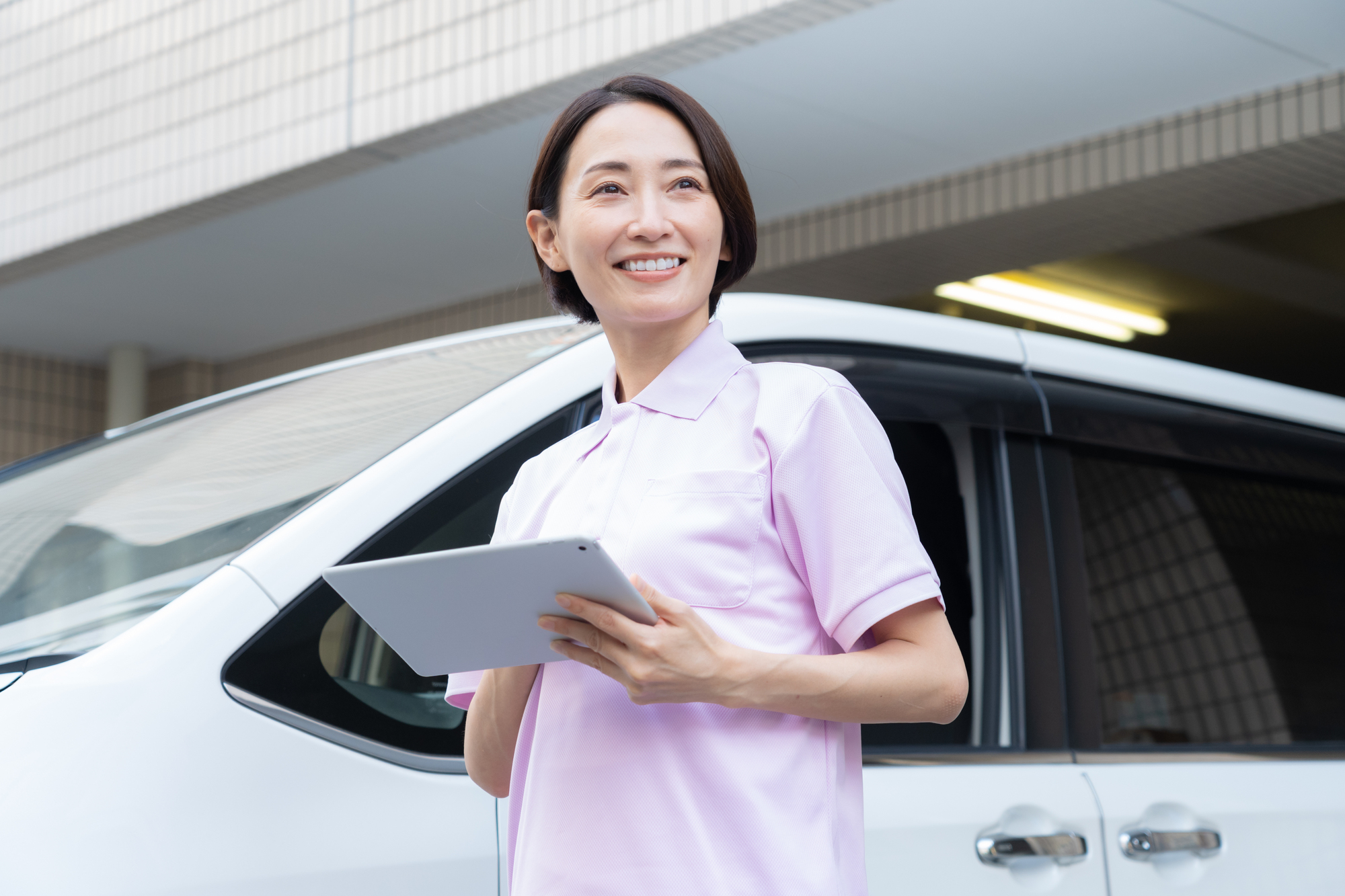 訪問先へ向かう車の脇でタブレットを手にしている訪問介護のスタッフ