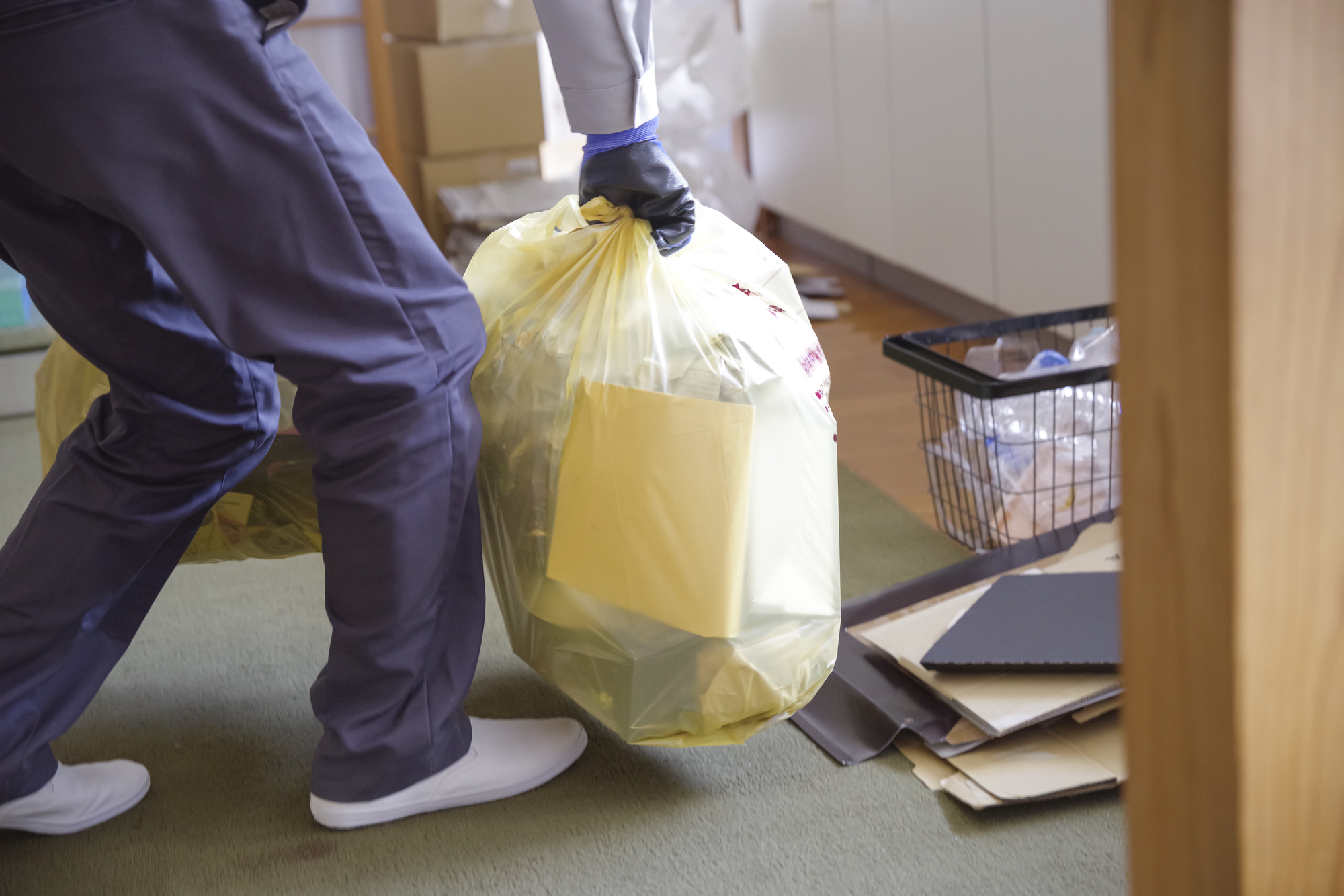 家の片付けの現場で、作業着の人が不用品を入れたごみ袋を運び出している