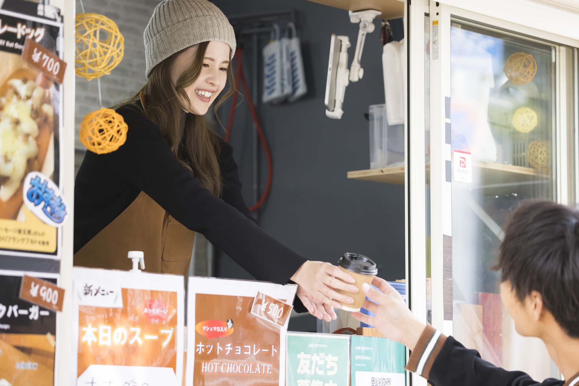 キッチンカーの窓口で、店員がホットの飲み物を客に手渡している