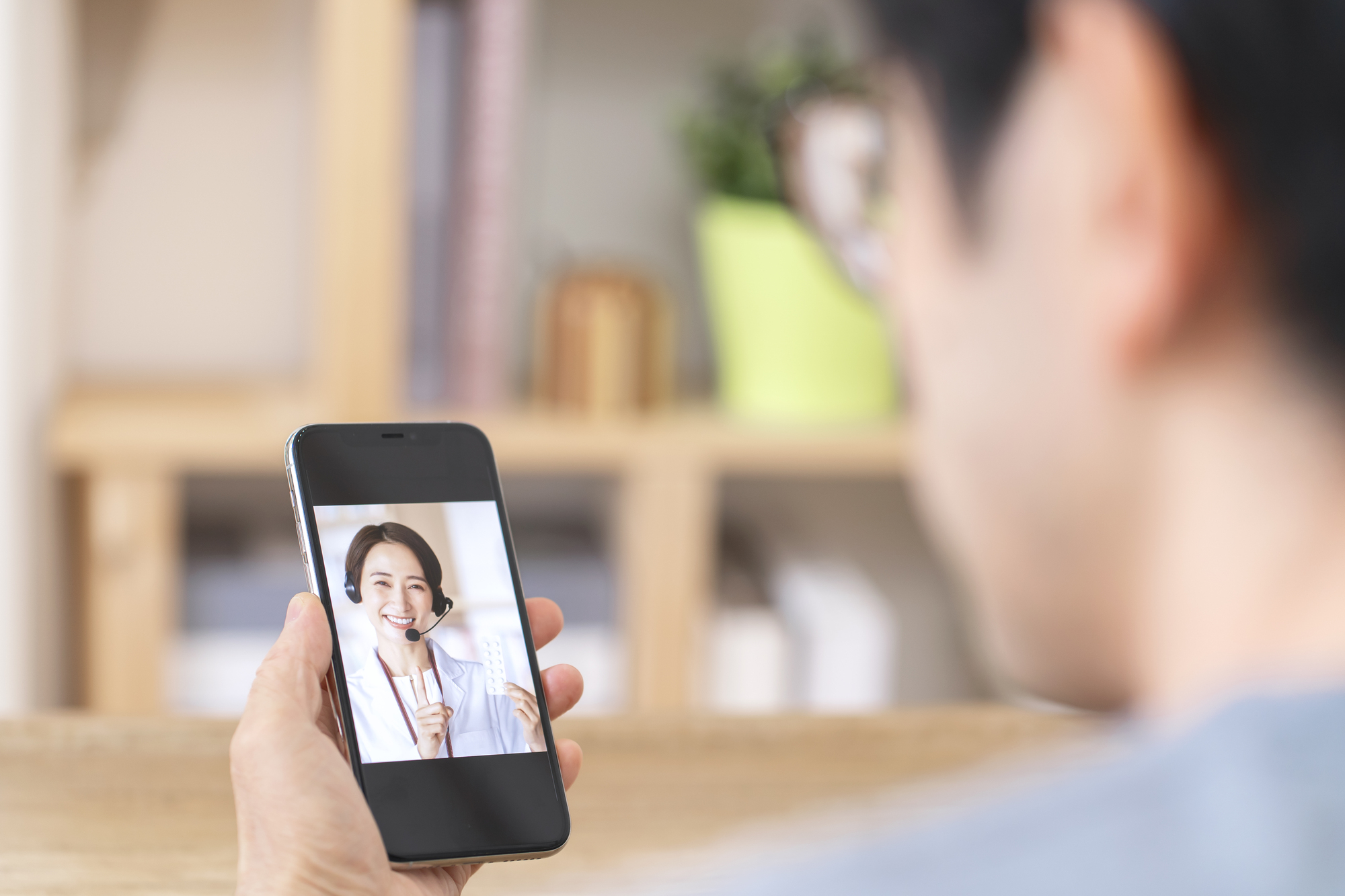 スマートフォンの画面越しに、ヘッドセットをつけた白衣の担当者から薬の説明を受ける人
