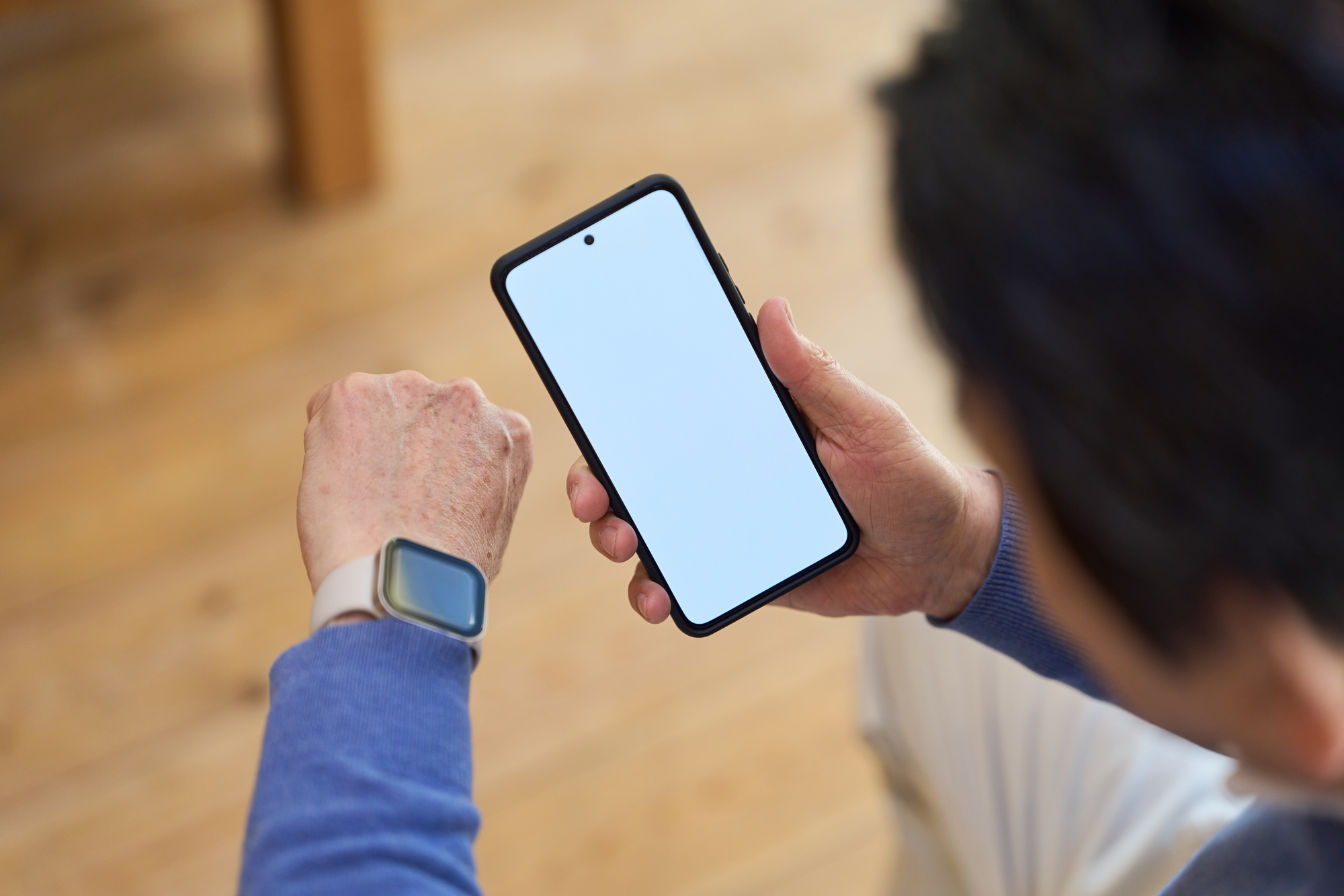 スマートウォッチを腕につけたままスマートフォンの画面を見ている手元