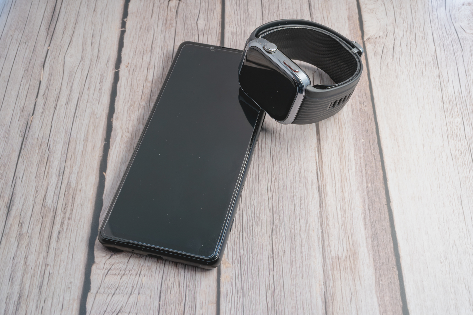 木目のテーブルに並べて置かれたスマートフォンとスマートウォッチ