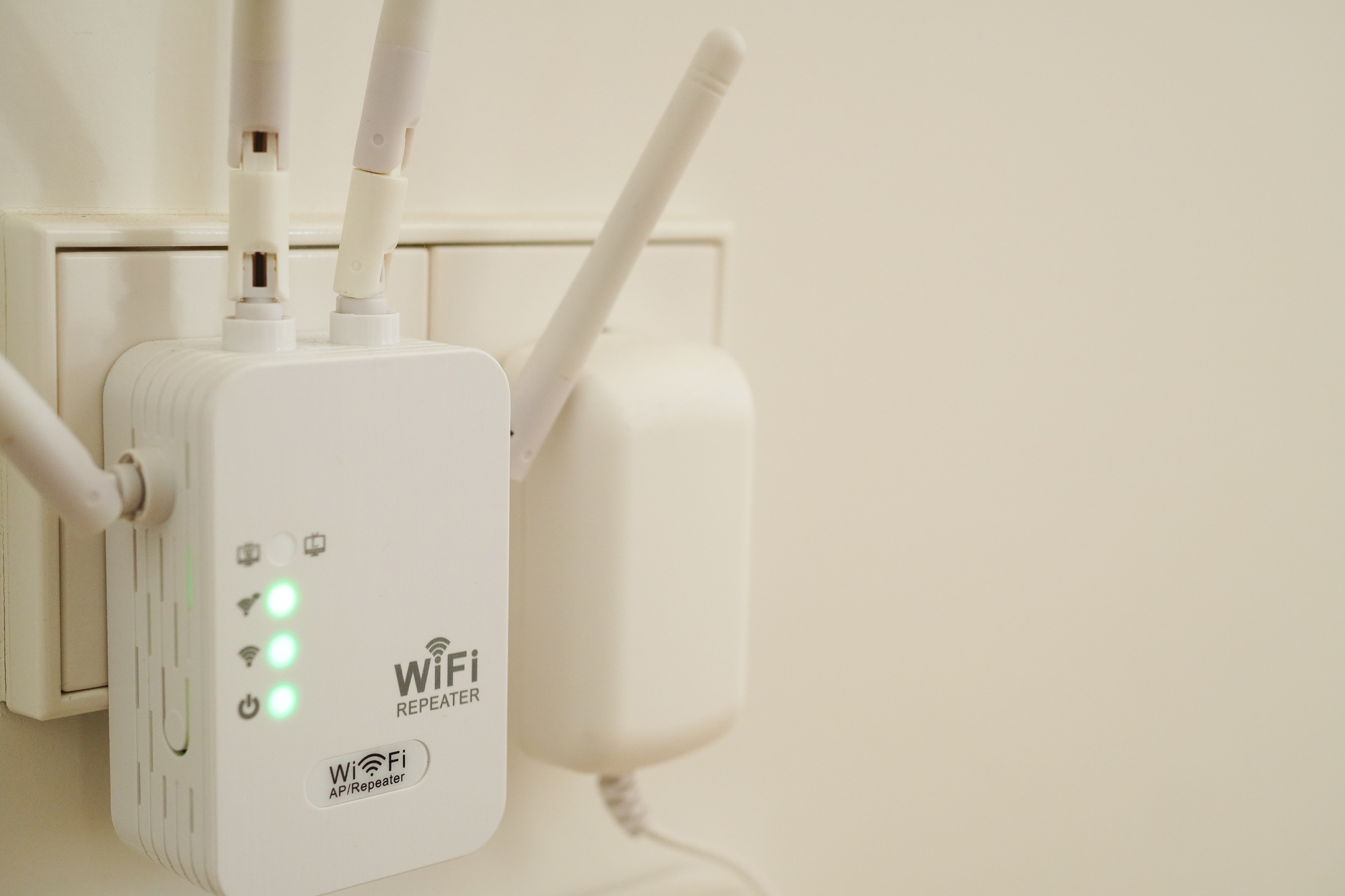 壁のコンセントに差し込まれた白い中継器。アンテナが立っている